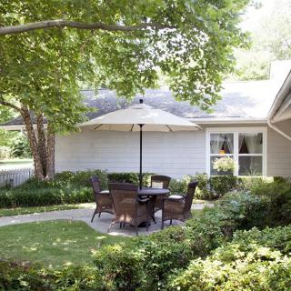 A serene backyard patio featuring outdoor seating under a large umbrella, surrounded by lush greenery and well-maintained landscaping.