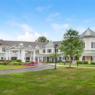 A large, elegant residential building with classic architecture and surrounding greenery under a clear blue sky.