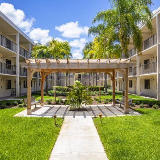 A beautifully landscaped apartment complex courtyard featuring a pergola and palm trees on a sunny day.
