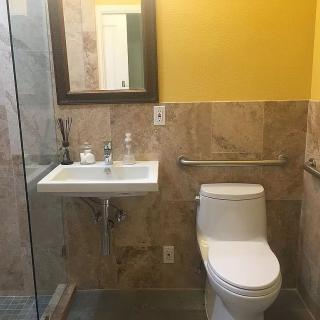 A modern bathroom with a toilet, sink, and mirror, featuring tiled walls and a yellow accent wall.
