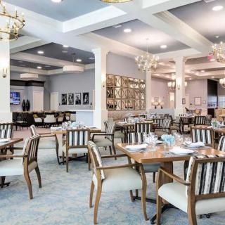 A spacious and elegantly designed dining area with neatly arranged tables and chairs, illuminated by chandeliers.