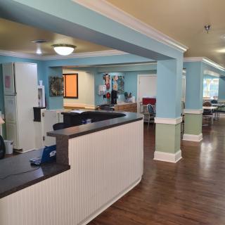 A spacious and welcoming nursing home reception area with light blue walls and wood flooring.