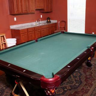 A game room featuring a pool table with a rich wooden finish and green felt, complemented by cabinets in the background.