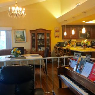 A cozy living space featuring an open floor plan that combines a living room, dining area, and kitchen, complete with a piano and elegant chandelier.