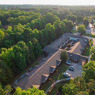 Aerial view of a building complex surrounded by lush forest and bathed in sunlight.