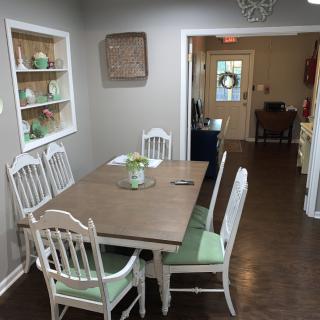 A cozy dining room with a wooden table and white chairs, featuring decorative shelves on the wall.