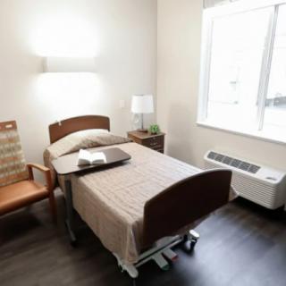 A hospital room with a single bed, chair, and natural light from a window.