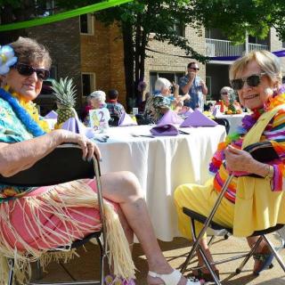 A lively outdoor party with a Hawaiian theme, where seniors are enjoying themselves with leis and colorful attire.