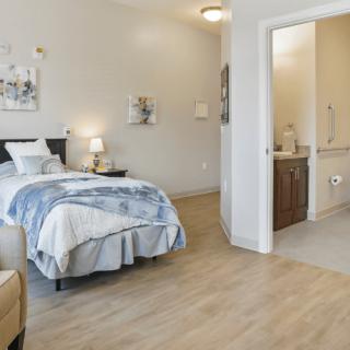 A modern and cozy bedroom with wooden flooring, featuring a neatly made bed and an adjoining bathroom.