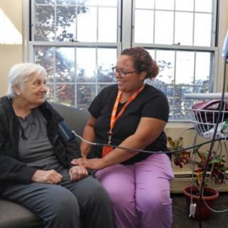 A nurse checks the blood pressure of an elderly patient in a cozy room setting.