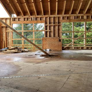 Unfinished building interior with wooden framing and large windows.