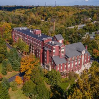 Aerial view of a large brick building surrounded by autumn trees.