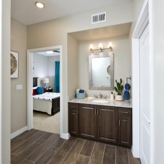 A modern bathroom with a sink and mirror, adjacent to a bedroom.