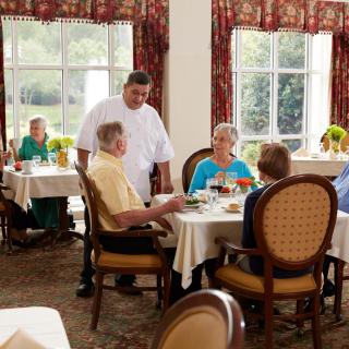 A group of seniors dining in a restaurant with a waiter attending to their table.