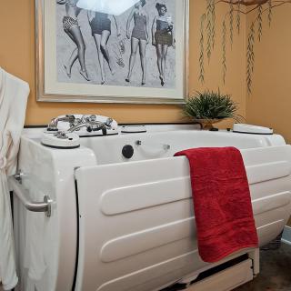 A bathroom featuring a walk-in bathtub with a red towel draped over the side, decorated with artwork and an indoor plant.