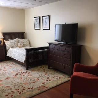 A cozy bedroom with a single bed, television, dresser, and an armchair.