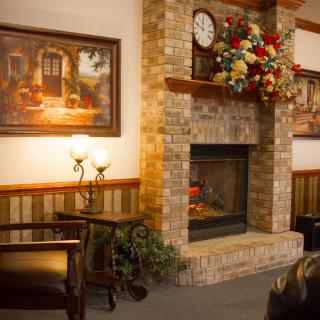 A cozy room with a brick fireplace, adorned with flowers and a clock, alongside elegant lamps and seating.