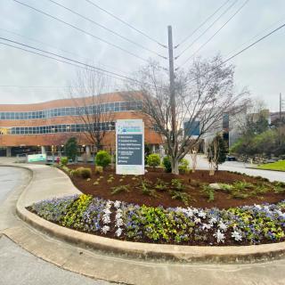 A hospital building with a landscaped entrance and directional sign on a cloudy day.