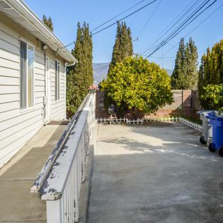 A concrete driveway beside a house, lined with trees and recycling bins under a clear sky.