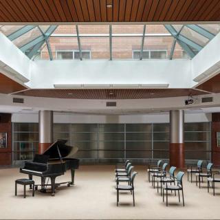 An empty concert hall with a grand piano and rows of chairs under a skylight.