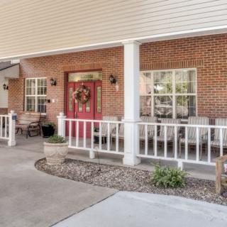 A welcoming porch with a vibrant red door, surrounded by brick walls and white railings.