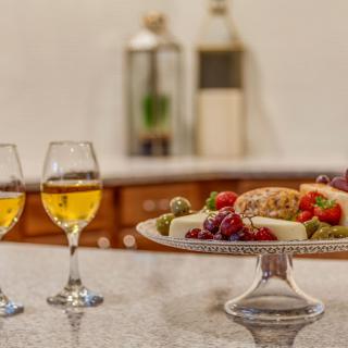 A gourmet platter with cheese and fruits paired with two glasses of white wine on a kitchen counter.
