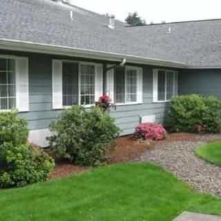 A residential house with well-maintained landscaping, featuring a lush green lawn and shrubs along a stone pathway.