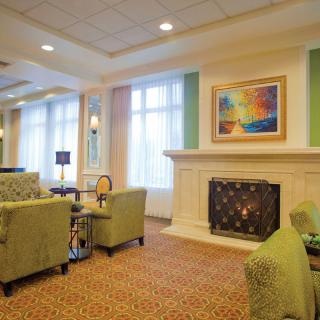 A cozy living room with green sofas and a fireplace, featuring colorful artwork above the mantel.