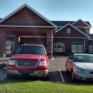 A sunny day at a parking lot featuring a red truck and a gray car in front of a well-constructed building.