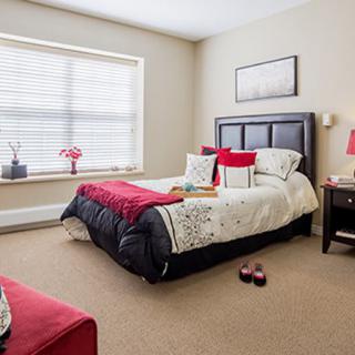 A cozy bedroom with red accent pillows and decor, featuring a large window and bedside lamps.