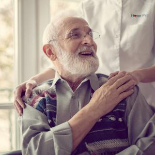 An elderly man smiling warmly as a caregiver offers support with a gentle touch.