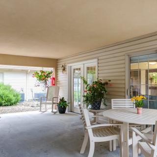 A cozy patio with a table, chairs, and vibrant plants under a sheltered area.