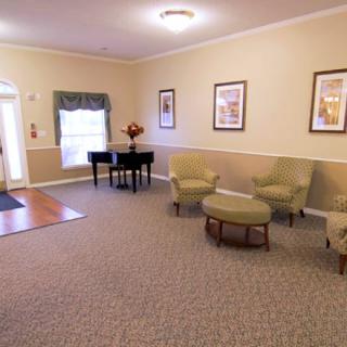 A cozy living room featuring comfortable seating, a piano, and framed artworks on the wall.