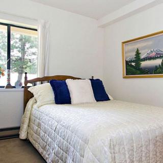 A cozy bedroom with a neatly made bed, featuring blue and white pillows, next to a window and adorned with a landscape painting on the wall.
