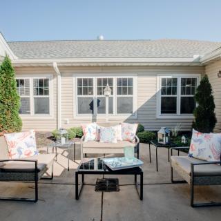 A cozy outdoor patio area featuring modern garden furniture set against a house exterior on a sunny day.