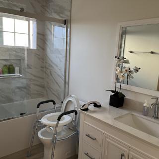A modern bathroom with an accessible toilet featuring grab bars, a sink, and a shower area.