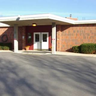 The image shows a brick building entrance with double doors and a driveway.