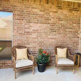 A cozy outdoor patio with two chairs and a potted plant against a brick wall.