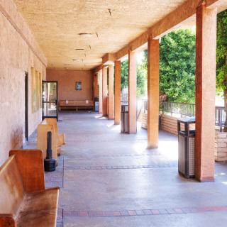 A sunlit outdoor corridor with wooden benches and columns.