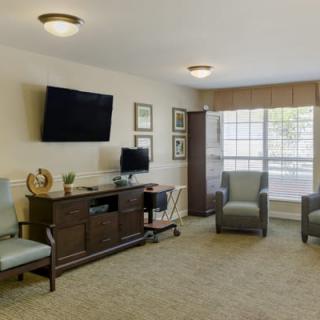 A cozy living room setting with chairs, a television, and ample natural light from a large window.