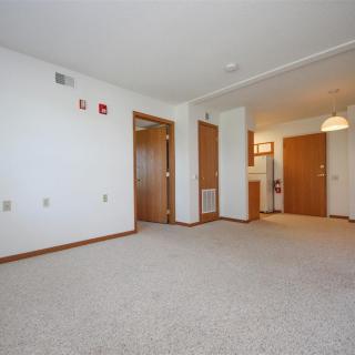 A spacious, empty living room with carpeted flooring and multiple wooden doors.