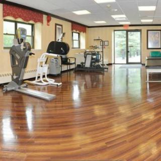 An empty gym with various exercise equipment and a polished wooden floor.