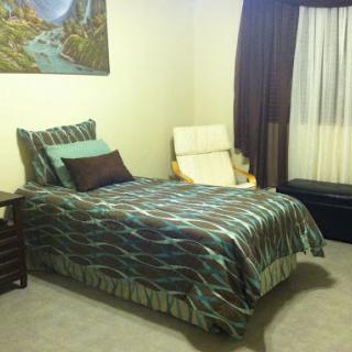 A cozy bedroom featuring a neatly made bed, decorative pillows, a comfortable chair, and natural light from the window.