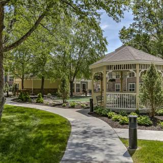 A peaceful park scene featuring a gazebo surrounded by lush greenery and trees, with a winding pathway.