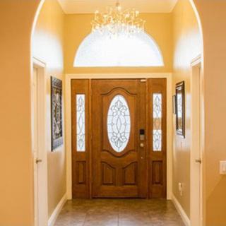 A warmly lit hallway leading to a wooden front door with glass panels, featuring a small chandelier overhead.