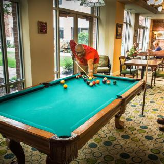 A person sets up a game of billiards on a pool table in a well-lit indoor recreational area.