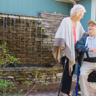 An elderly couple enjoying time together outdoors by a fountain.