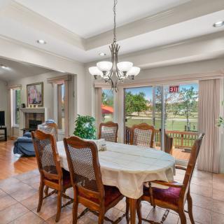 A well-lit dining room featuring a large table with chairs and a chandelier, overlooking a scenic backyard through wide sliding glass doors.