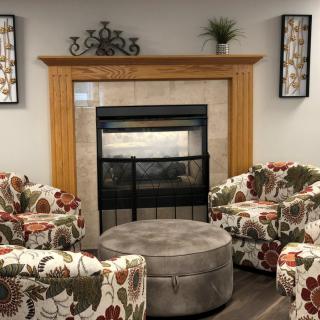 A cozy living room with a central fireplace surrounded by floral armchairs and a plush coffee table.