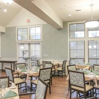 A neatly arranged dining room with several tables and chairs, featuring large windows and elegant decor.